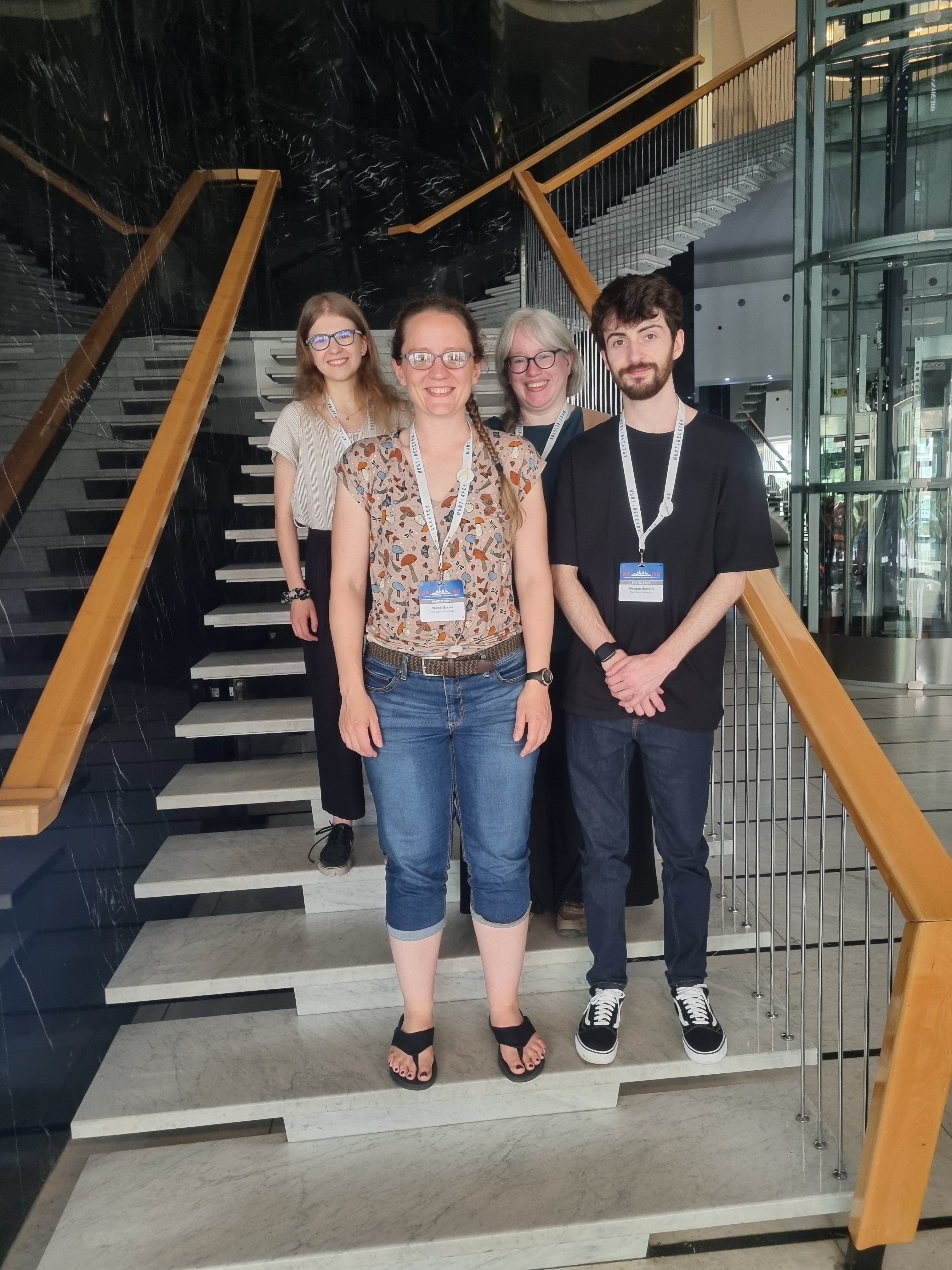 Four happy looking people on a stairwell wearing conference lanyards. They look nerdy and delighted, and it's not dissimilar to a family photo of awkward people who genuinely like each other. The individuals are Julia, Wendi, Marisa, and Morgan.