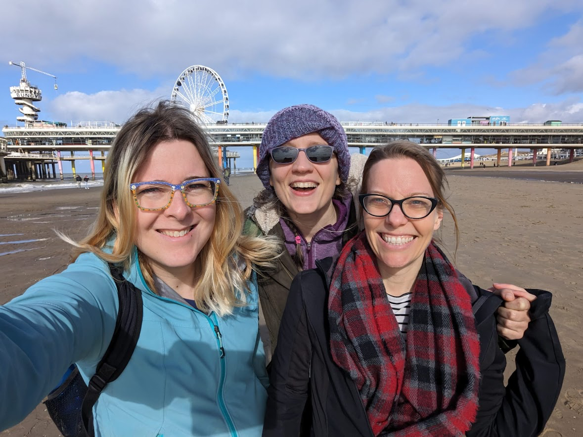 Three happy looking people on a beach with a ferris wheel in the background. Everyone is wearing glasses and clearly a nerd. The individuals are Helena, Saskia & Wendi